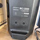 Zadní strana černého reproduktoru s texturovaným povrchem. Na stříbrném štítku je uveden název DEXON a model BC 1200, dále technické parametry, sério…