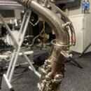 Detailní záběr na horní část saxofonu stříbrné barvy. Nástroj vykazuje viditelné opotřebení povrchu v podobě tmavších skvrn a znečištění. Na hřebenu…