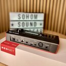 Černý elektronický přístroj s nápisem REDNET na horní straně, umístěný na bílém kartónovém boxu s červeným pruhem a nápisy Focusrite, Dante a REDNET.…