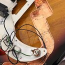 Fotografie zachicuje vnitřní část elektroiky elektrické kytary s tělem v provedení sunburst. Je vidět bílá pickguard s připojenými snímači a potencio…