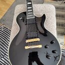Černá elektrická kytara s tvarem single-cutaway a bílým lemováním hran. Nástroj má dva humbuckery, zlatý most a strunovník, čtyři černé ovládací knof…