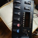 Černý kytarový procesor s nápisem GT-100 EFFECTS PROCESSOR a logem BOSS. Zařízení obsahuje několik stoupacích spínačů označených čísly 1 až 4, tlačít…
