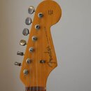 Zadní strana hlavy dřevěné elektrokytary v přirozené žlutohnaté barvě. Na zadní straně je černý nápis Fender STRATOCASTER a v horní části text Origin…