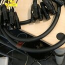 Sada černých audio kabelů s více konektory typu XLR. Některé kabely mají žluté papírové štítky s nápisy VOC1, CS a KYZ. Na povrchu některých kabelů j…