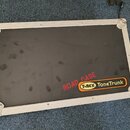 Černý transportní kufr s hliníkovým rámem a kovovými rohy. Na povrchu je červený nápis ROAD CASE a logo T-REX ToneTrunk v žlutém oválu. Povrch kufrů…