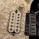 Detail elektrické kytary s bílým perleťovým pickguardem. Je vidět humbucker s bílými cívkami a nápisem Seymour Duncan, kovový most a dva bílé ovládac…
