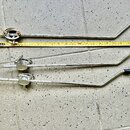 Tři kovové chromované ramena mikrofonních stativů s černými plastovými rukojtěmi. Vedle horního ramene je položen žlutý metr. Na kovových površích js…