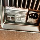 Detail zadní strany černého elektronického zařízení s chladicími žebry. Je zde vypínací tlačítko s nápisem ON a vstup pro napájecí kabel. Na štítku j…
