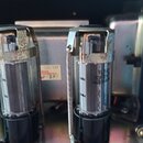 Detail vnitřku elektronického zařízení s dvěma elektronkami v kovových držácích. Na jedné z elektronek je čitelný nápis EL34, SOVTEK a MADE IN RUSSIA…