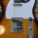 Elektrická kytara s tělem v provedení sunburst a bílým pickguardem. Nástroj má chromovaný most s kobylkou a ovládací panel s přepínačem a dvěma knofl…