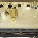 Zadní strana elektronického zařízení s kovovým panelením. V horní části jsou rozmístěny různé typy konektorů, včetně tří černých kulatých s více piny…