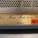 Detail zlatavého kovového štítku na hudebním přístroji. Na štítku je kurzívou napsán text Mk 2. Master Model 100w Lead. a níže nápis SERIAL NO: S/A.…