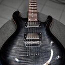 Elektrická kytara s tmavým, žilnatým povrchem těla a hnědým hnedem hmatníkem. Nástroj má dva humbuckery, most s úhlovým laděním a dvě otočné knoflíky…