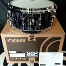 Tmavě modrý buben s chromovaným obručováním a ladicími šrouby. Nástroj stojí na hnědé papírové krabici s nápisy SONOR Made in Germany a SQ2 DRUM SYST…