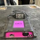 Šedý plastový přístroj s růžovými prvky a nápisem CUETY. Na zadní straně jsou viditelné konektory označené jako ETHERNET a DMX-512. K přístroji je př…