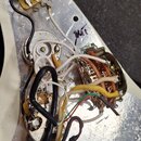 Fotografie zachycuje vnitřek elektroniky elektrické kytary s kovovou stíněnou vrstvou. Jsou vidět tři potenciometry, kondenzátor a spínací prvek s mn…