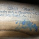 Detail vnitřní štítku hudebního nástroje s nápisem v němmeckém písmu: „210 am Martin macht mich in Reutlichen, im Baigh land beg Aborf. Ao 17“. Pod š…