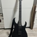 Černá elektrická kytara s matným povrchem a černým hardwarem. Na hlavě je viditelné logo "Ibanez". Kytara má dva humbuckery, jeden ovládací knoflík a…