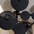 Elektronická bicí souprava v černé barvě. Na dvou horních činely je viditelné logo YAMAHA. Souprava obsahuje několik padů a pedály, povrchy jsou v ma…