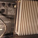 Zadní strana černého zesilovače s velkým hliníkovým chladičem v pravé části. Jsou zde viditelné nápisy SPEAKERS, POWER AMP 2, BRIDGE a POWER AMP 1 sp…