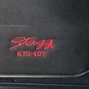 Detail černé látkové krycí mřížky reproduktoru. Na povrchu je červeným vyšívaným písmem nápis Stagg a pod ním označení modelu KTC-107. Látka vykazuje…