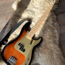 Elektrická basová kytara s tělem v provedení sunburst a zlatým pickguardem. Na hlavě hředu je viditelné logo Squier. Nástroj má světlou dřevěnou hmat…
