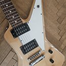 Elektrická kytara s přírodním dřevěným povrchem a bílým plechtrátem. Nástroj má dva černé humbuckery a chromovaný most. Na spodní části těla je vidit…