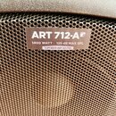 Detailní záběr na hnědou kovovou mřížku reproduktoru. Na mřížce je nalepená bílá nálepka s nápisy ART 712-A MK4, 1400 WATT · 129 dB MAX SPL a SUPERIO…