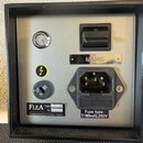 Zadávací panel elektronického zařízení s šedým povrchem a černým rámem. Panel obsahuje vypínač, kontrolku, zásuvku pro napájecí kabel s nápisem MAINS…