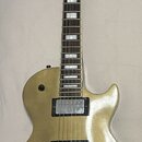 Zlatá elektrická kytara s dvěma humbuckery a čtyřmi ovládacími knoflíky. Na hlavě nástroje není žádný viditelný nápis ani logo. Povrch těla vykazuje…
