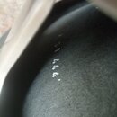Detailní záběr na tmavý, matný povrch předmětu. Na povrchu jsou viditelné drobné světlé stopy a nečitelné bílé znaky. Fotografie je rozostřená.