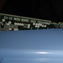 Fotografie zachycuje zelenou tiskovanou plošnou desku s elektronickými součástkami, která vyčnívá z modrého plastového šasi. Na desce jsou bílé nápis…