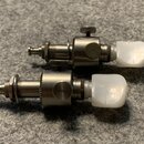Dvě ladicí mechaniky s kovovým tělem a bílými plastovými knoflíky. Povrch kovu vykazuje známky opotřebení a drobné škrábance. Na dílech nejsou žádné…