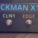 Černý kytarový procesor s nápisem ROCKMAN X100 v modré barvě. Pod ním jsou čtyři přepínače s barevnými popisky: modrý CLN2, zelený CLN1, oranžový EDG…