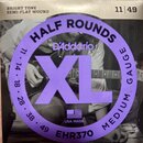 Fotografie balení kytarových strun s fialovou kulatou nálepkou. Na nálepce jsou nápisy HALF ROUNDS, D'Addario, XL, MEDIUM GAUGE a EHR370, dále je zde…