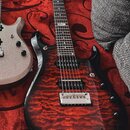 Elektrická kytara s červeným plamenovitým povrchem těla a černým hmatníkem. Na 12. pražci je viditelné logo "Ibanez". Kytara má dva humbuckery, chrom…