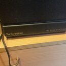 Černý reproduktor s látkovou maskou. Na spodní části je bílým nápisem značka Schneider a text WIDE RANGE SPEAKER SYSTEM. Povrch spodní části vykazuje…