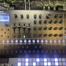 Černý syntetizátor s nápisem Roland SYNTHESIZER SH-4d. Přístroj obsahuje displej s textem PRESET RING, několik posuvníků a otočných knoflíků rozdělen…