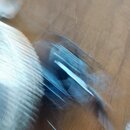 Fotografie je extrémně rozmazaná a neostrá. Je na ní vidět modrý předmět s bílým prvkem na hnědém podkladu, pravděpodobně dřevěné podlaze. Žádné znač…