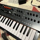 Klávesový synthesizátor s černým šasi a ovládacími prvky v horní části. Na pravé straně je nápis MINITEK. Panel obsahuje různé potenciometry, přepína…