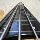 Detailní pohled na hриф basové kytary s černým hmatníkem a čtyřmi strunami. Na hmatníku jsou vidět bílé tečkové značky poloh. Krk nástroje je vyroben…