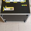 Černý flightcase s osazením elektroinstalace. Horní panel obsahuje řadu jističů a žluté nápisy PHASE, SCHALTER-OUT(1), SCHALTER-OUT(2) a LED LIGHT. S…