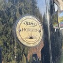 Detail černé lesklé povrchové vrstvy bubnu s kruhovým dřevěným štítkem. Na štítku je uveden nápis MAPEX v oválu a pod ním slovo HORIZON, doplněno gra…