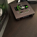 Černý zvukový interface s nápisem apollo twin a logem UNIVERSAL AUDIO. Zařízení má velký stříbrný ovládací knoflík s podsvícením a řadu malých tlačít…