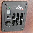 Černý ovládací panel s nápisem SIGMA a logem ve tvaru řeckého písmene sigma. Panel obsahuje digitální displej, tlačítko TUNER, ovrtět VOLUME a tři po…