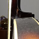 Detailní pohled na spoj hřdelníku s tělem akustické kytary v tmavě hnědé barvě. Na povrchu lakovaného dřeva jsou viditelné škrábance a drobné oděrky.…