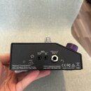 Zadní strana černého elektronického zařízení s několika konektory. Jsou zde nápisy MIDI OUT, MIDI IN a CTL 4, 5/ EXP 2. V levé dolní části je text Ro…