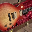 Elektrická kytara s tónem sunburst v červeně a žluté, umístěná v hnědém kufru s červeným plyšovým vnitřkem. Nástroj má dva humbuckery, čtyři otočné k…