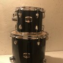 Dvě černé bubny s chromovanými obručmi a ladicími šrouby, které jsou na sebe naskládány. Oba mají zlatý oválný štítek s nápisy YAMAHA a GIGMAKER. Pov…