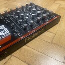 Synthesizér Roland PG 200 v červeno-černé barevné kombinaci. Na předním panelu jsou viditelné nápisy Roland, PG 200 a Synthesizer, spolu s řadou ovlá…